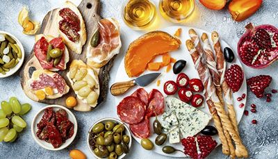 knife, breadsticks, persimmon, pomegranate, mimolette, appetizer, physalis, grapes, capers, olives, pickles, salami