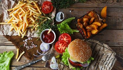 hamburger, zelenasolata, paradižnik, žemljica, vilica, čebula, časopis, kečap, sir, pomfri, sol